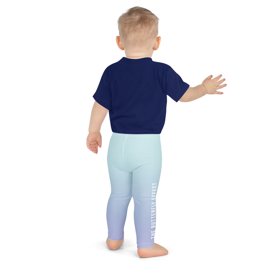 A baby viewed from the back wearing a navy blue t-shirt and light blue leggings with a vertical white text print reading 'THE BUTTERFLY EFFECT'.