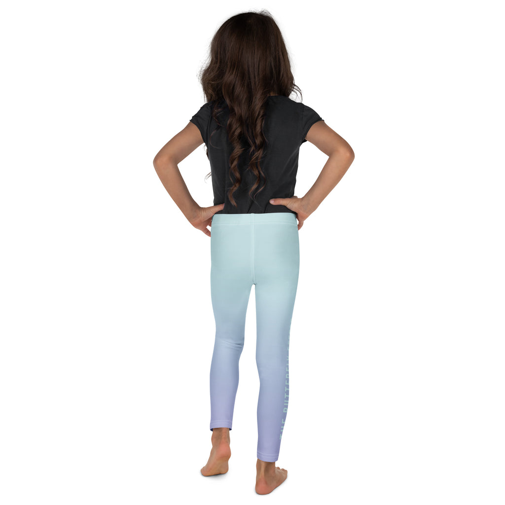 A child model shown from the back wearing light blue gradient leggings that fade to lavender-purple at the ankles, paired with a black t-shirt, on a solid white background.