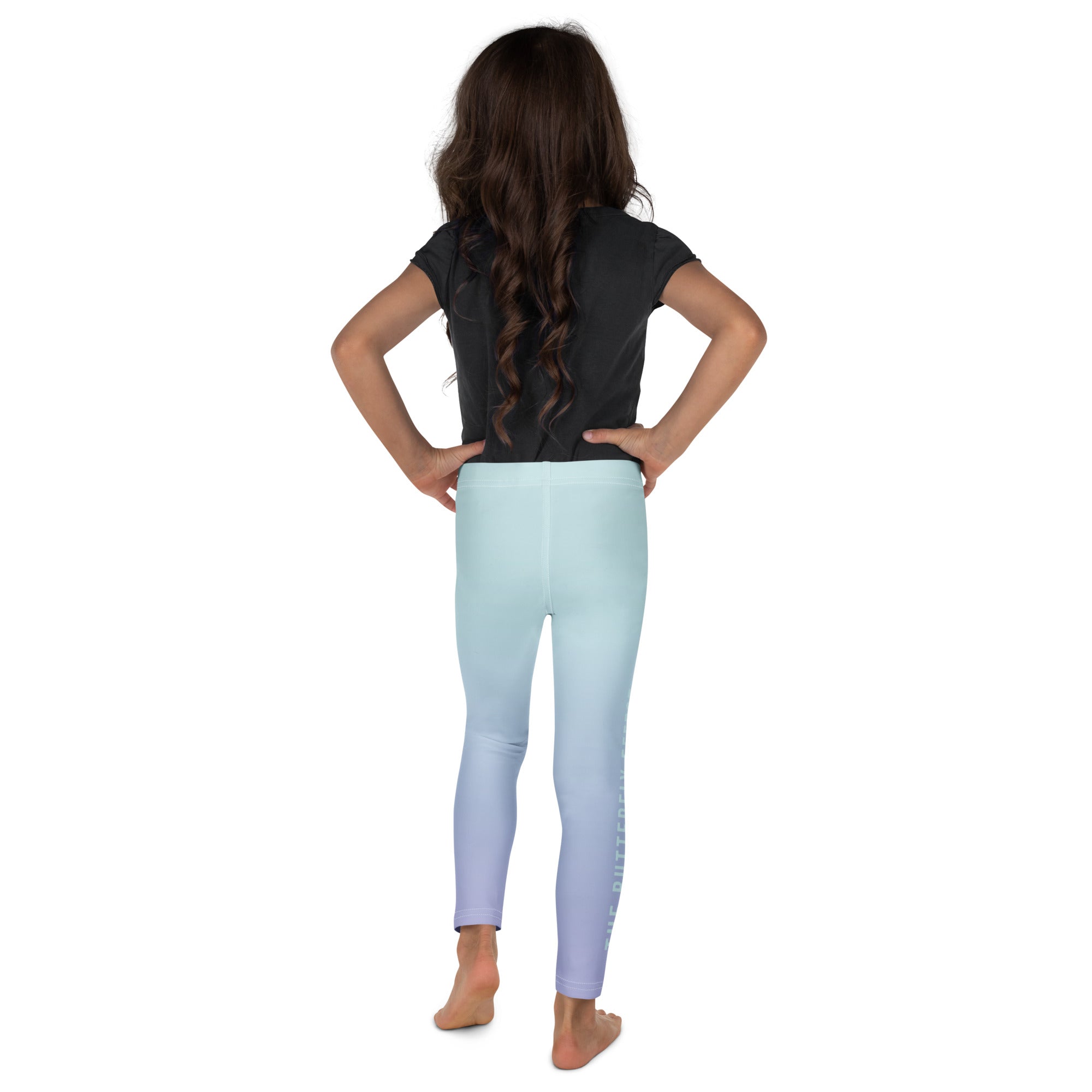 A child model shown from the back wearing light blue gradient leggings that fade to lavender-purple at the ankles, paired with a black t-shirt, on a solid white background.
