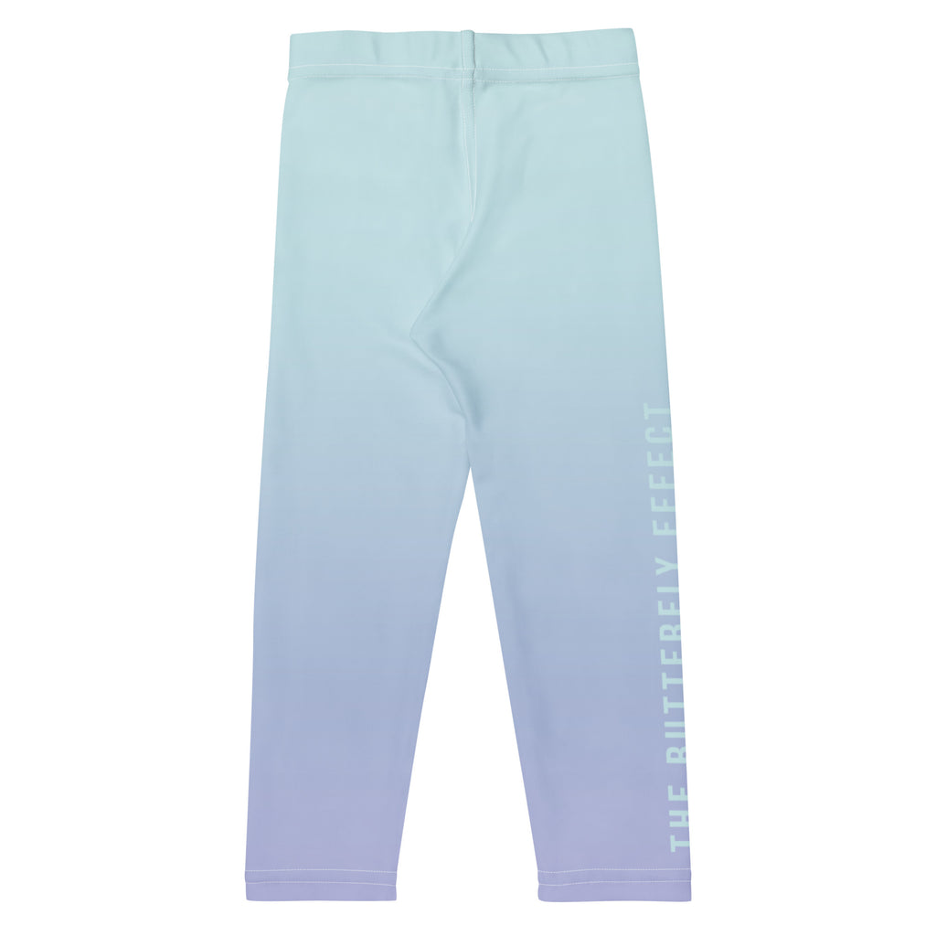 A pair of children's leggings with a vertical ombre gradient transitioning from light mint green at the top to soft lavender at the bottom, featuring 'THE BUTTERFLY EFFECT' printed vertically in white on the lower right leg.