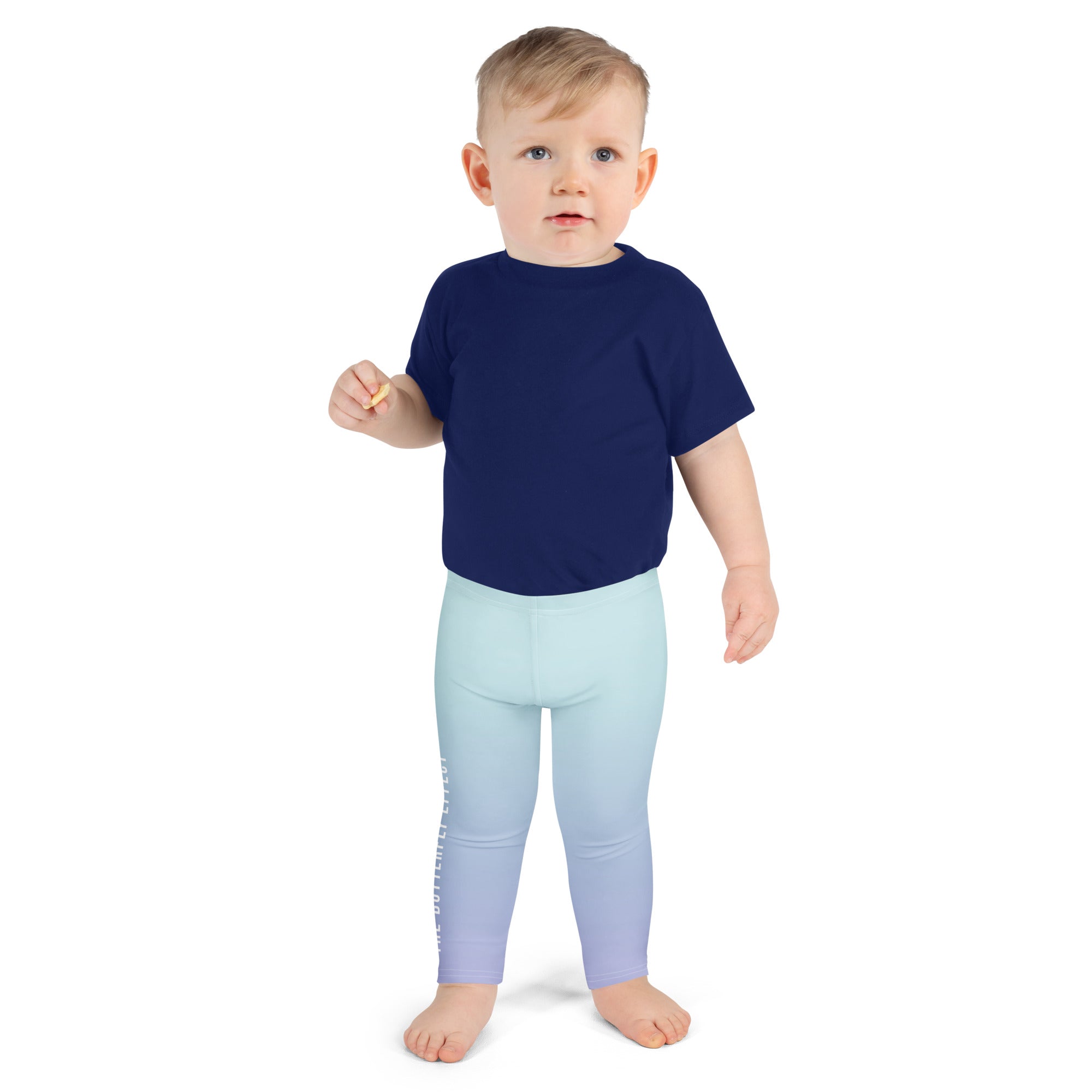 A toddler standing against a plain white background, wearing a navy blue short-sleeve t-shirt and light blue to lavender gradient leggings.