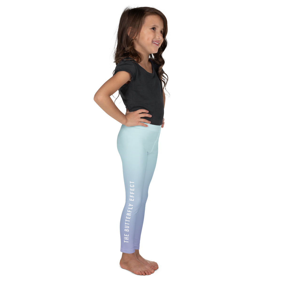 A young girl standing in profile wearing light blue gradient leggings with white vertical text reading 'THE BUTTERFLY EFFECT' and a black t-shirt, against a plain white background.