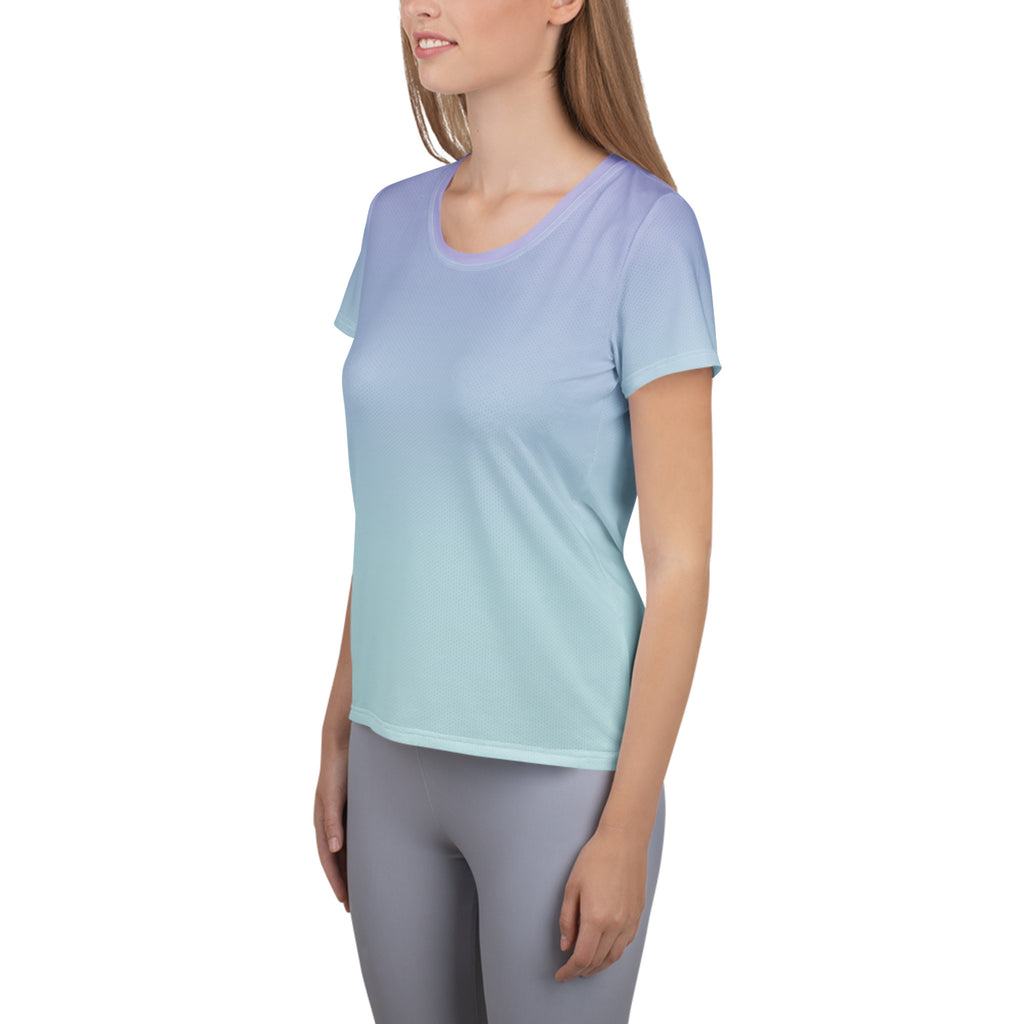 A woman wearing a short-sleeve athletic t-shirt with a smooth color gradient transitioning from light lavender purple to mint green, paired with gray leggings, shown against a plain white background.