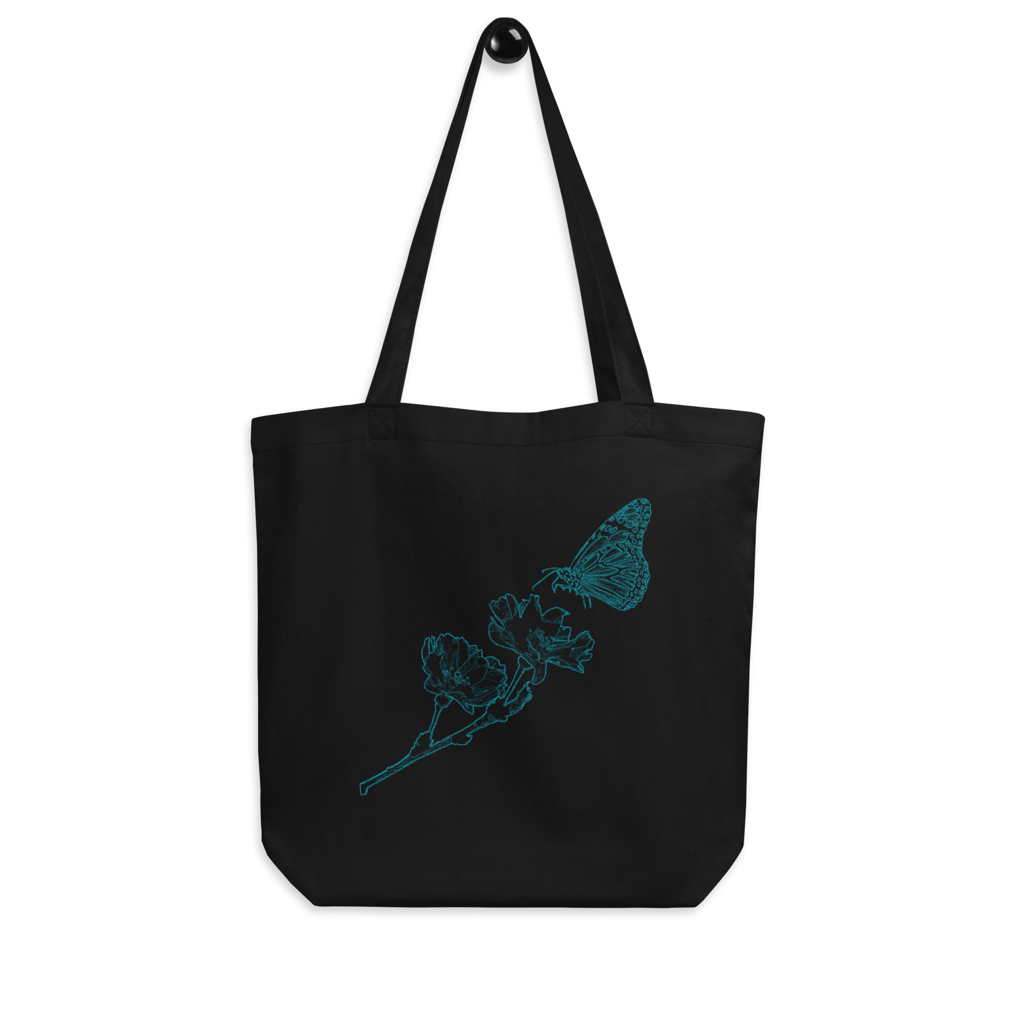 A black canvas tote bag with two shoulder straps, featuring a teal line art graphic of a butterfly and flower on the front, set against a plain white background.