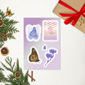 A sheet of decorative stickers displayed on a light background with holiday greenery, dried orange slices, cinnamon sticks, and a wrapped gift box. The stickers include a butterfly, a monarch butterfly, floral illustrations, and a patterned card design.