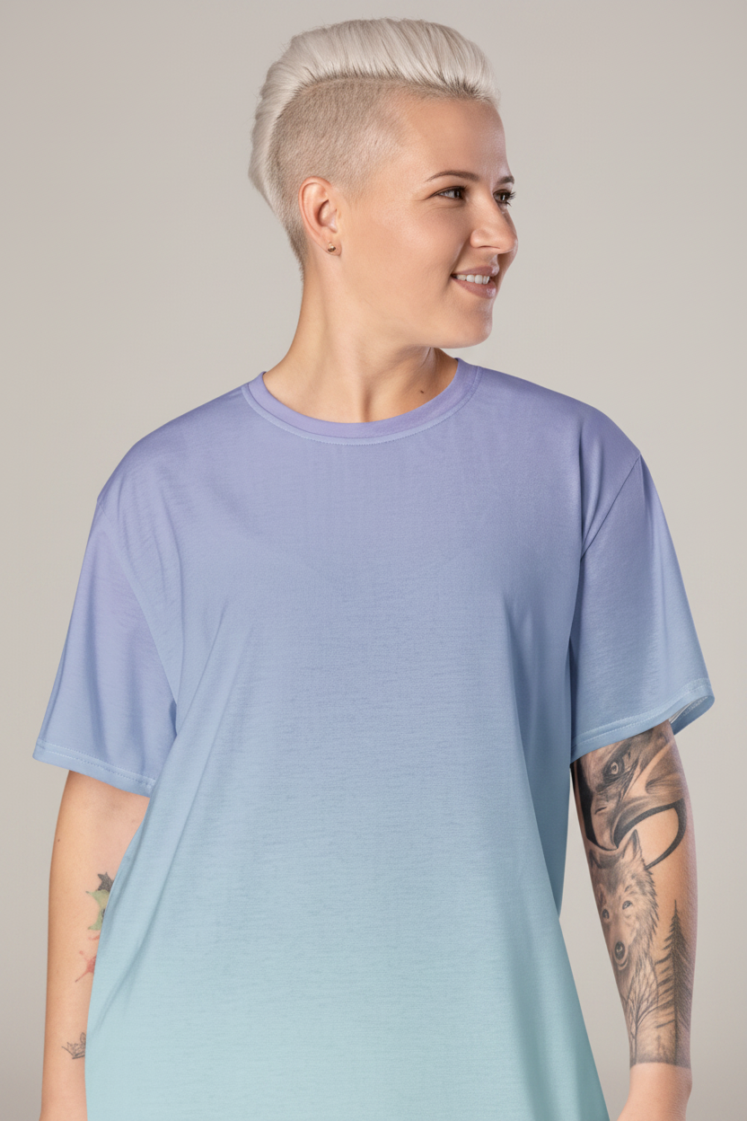 A model with short platinum blonde hair and visible tattoos wears an oversized short-sleeve crewneck t-shirt with a smooth color gradient transitioning from light periwinkle purple at the top to pale mint green at the bottom, set against a solid light gray studio background.